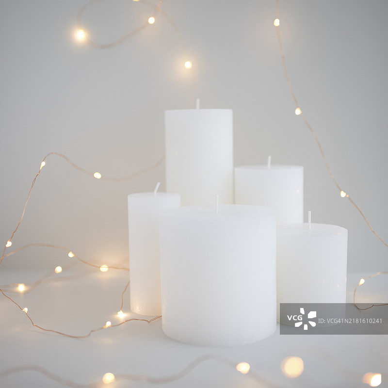 白色蜡烛周围的彩色灯光，灰色背景图片素材
