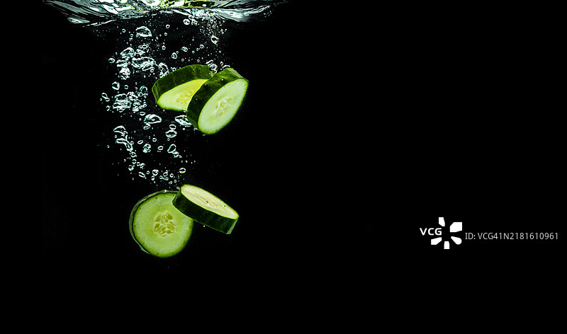 黑色背景的有机黄瓜切片水花飞溅，皮肤保湿化妆品概念图片素材