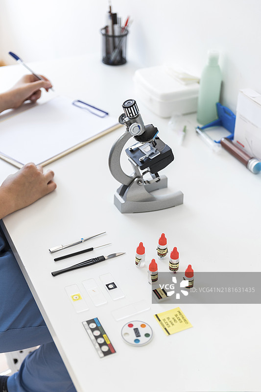 兽医在实验室的桌子上用显微镜书写病历板图片素材