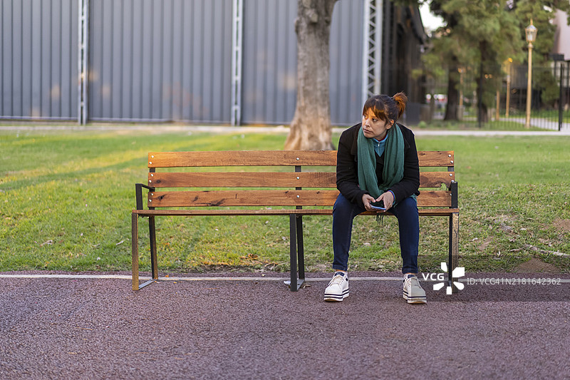 在公园长椅上用手机沉思的拉丁裔女子图片素材