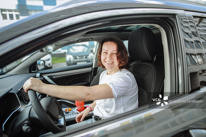 中年女性在新车的方向盘后微笑，满脸自豪图片素材