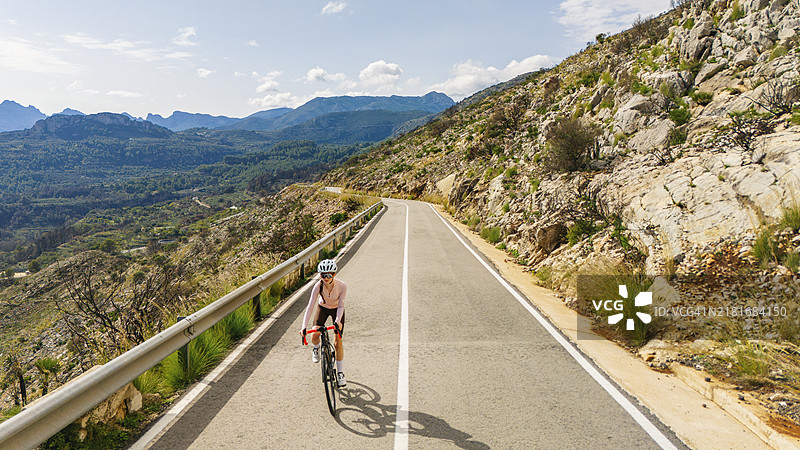 少女在西班牙山区骑公路自行车上坡的正面航拍图片素材