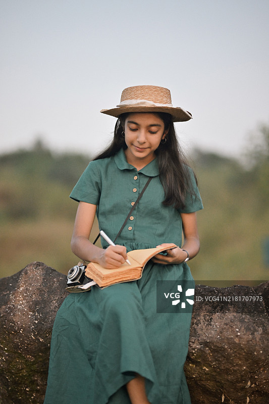 穿着复古裙子和草帽的女孩在大自然中写作图片素材