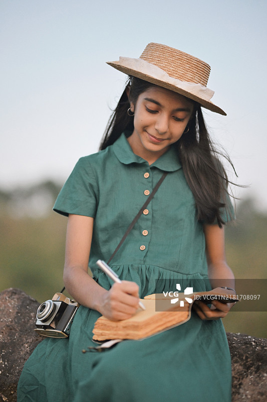 穿着经典亚麻绿色裙子和草帽的快乐女孩在大自然中写作图片素材