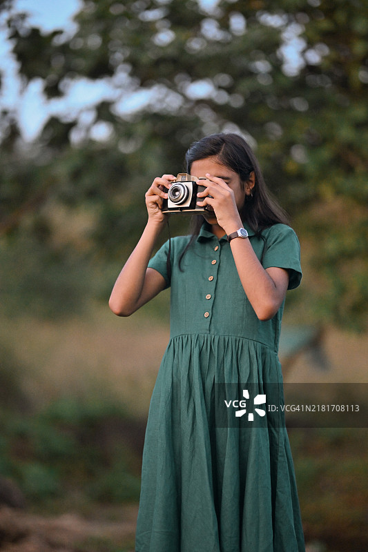 年轻女孩穿着经典裙子，用复古相机拍摄自然风光图片素材