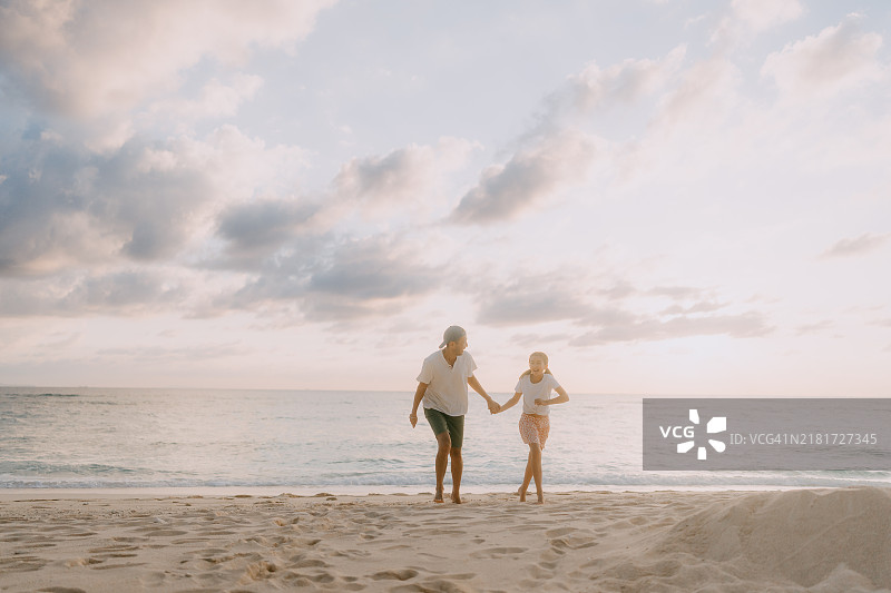 父亲和小女儿在日落时分的海滩上享受美好时光图片素材