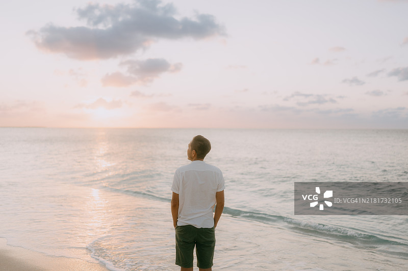 海滩上的男人，凝视着水面上地平线的日落图片素材