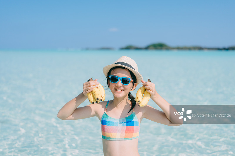 年轻女孩手持新鲜香蕉，站在清澈的热带水域，位于日本与论岛图片素材