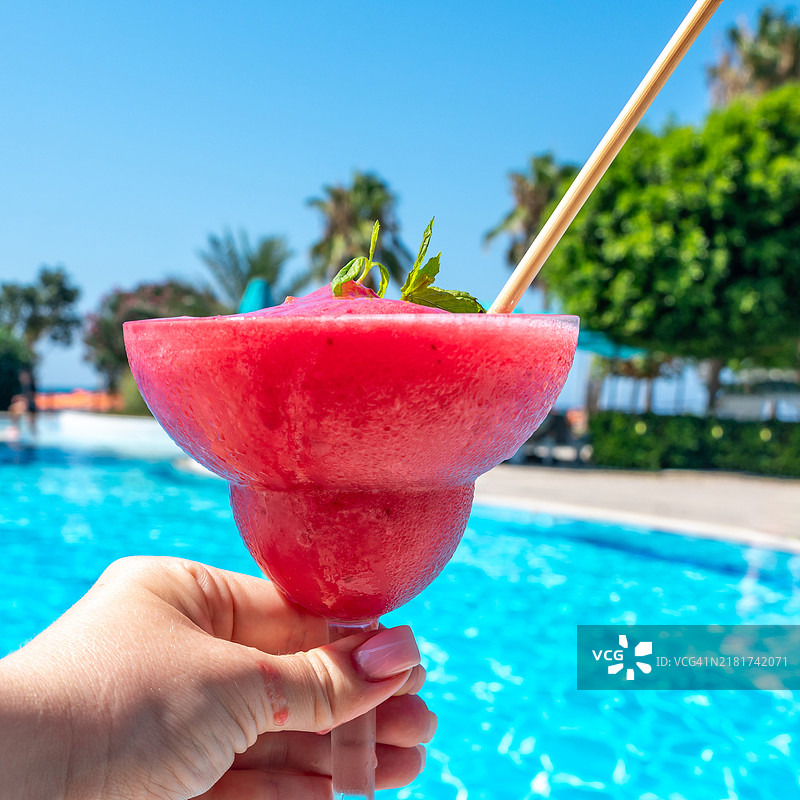 阳光明媚的泳池旁，手中拿着冰镇的覆盆子达基里和薄荷叶图片素材