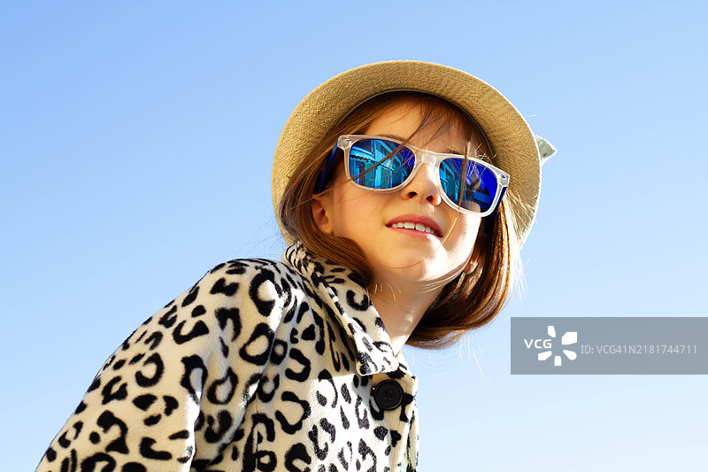 低角度视图的女孩戴着太阳镜，背景是晴朗的天空图片素材