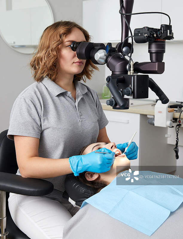 女牙医在牙科诊所使用显微镜为患者治疗牙齿图片素材