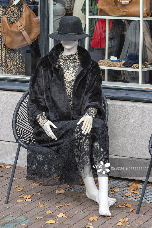 穿着黑色皮草外套和连衣裙的女人体模特坐在椅子上图片素材