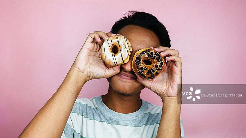 男人在粉色背景工作室中用眼睛托着甜甜圈图片素材