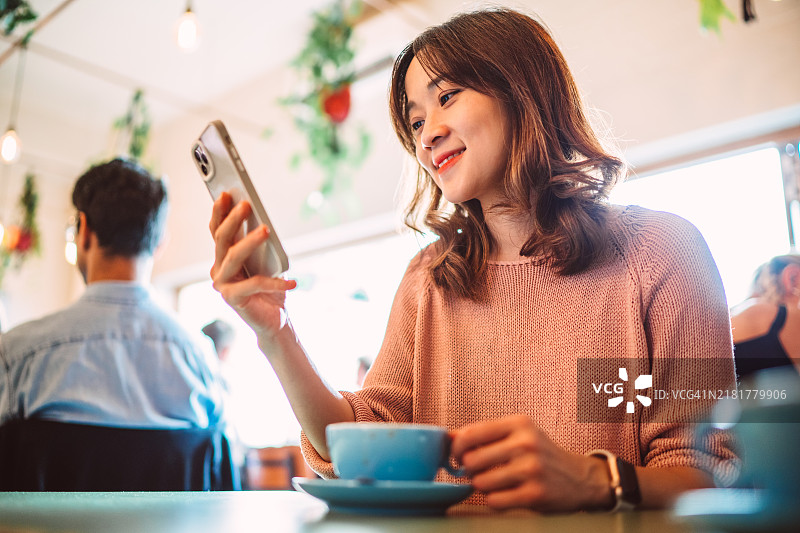 愉快的女性在咖啡馆享受咖啡休息时使用智能手机图片素材