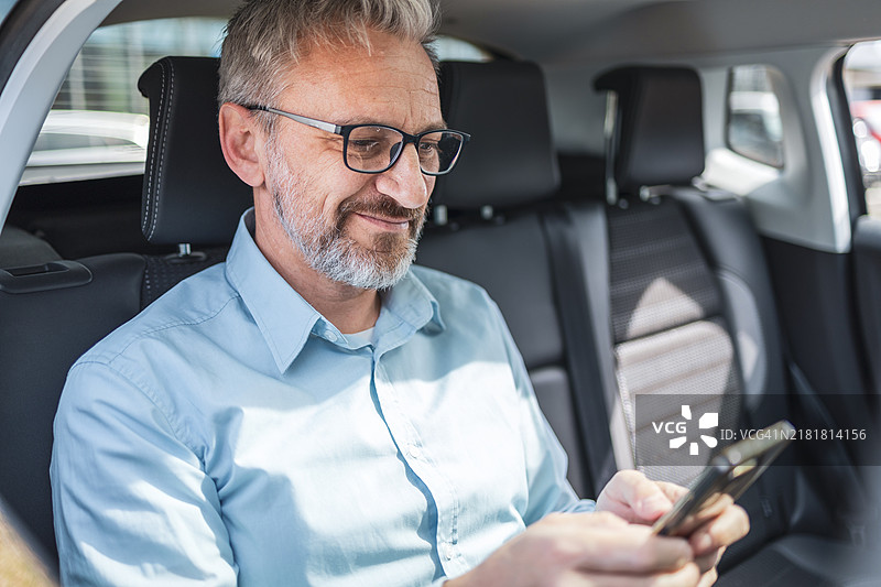 在出租车上用智能手机远程办公的成熟商人图片素材
