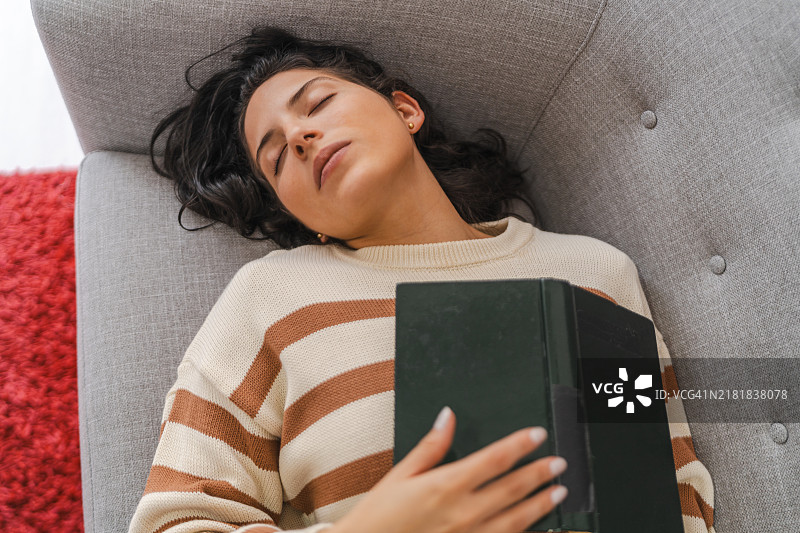 躺在沙发上，胸前放着一本书的睡觉女人图片素材