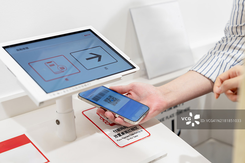 中年亚洲夫妇，中年亚洲女性在服装店的自助结账处使用智能手机进行非接触式支付。图片素材