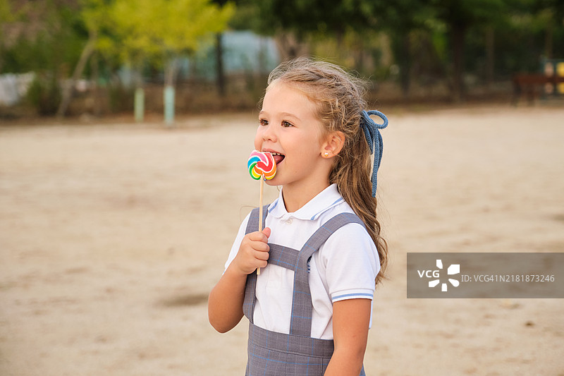 在操场享受彩色棒棒糖的女学生：童年的甜蜜与快乐图片素材