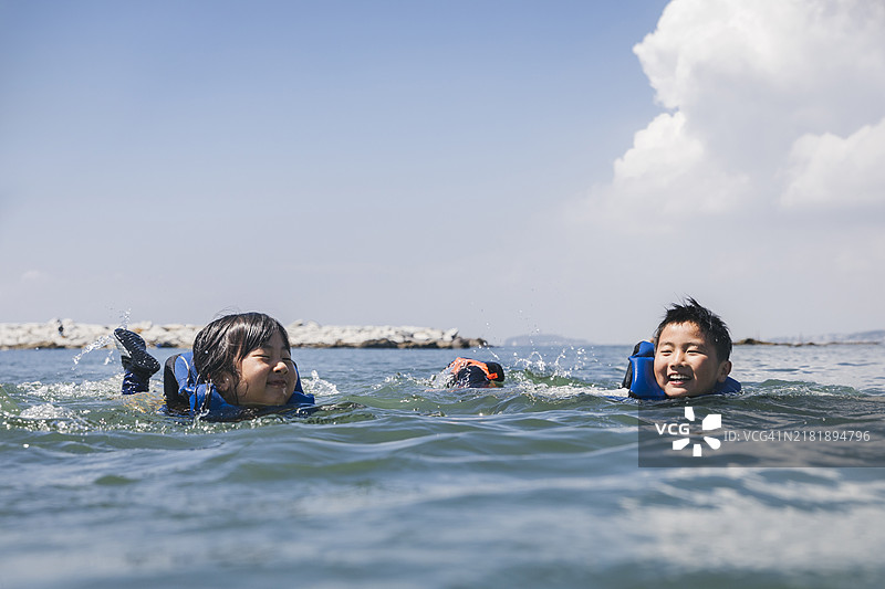 亚洲兄妹穿着救生衣在海中游泳图片素材
