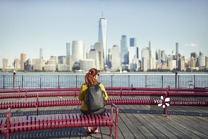 女人坐在长椅上，背对着曼哈顿天际线，欣赏纽约市的风景。图片素材