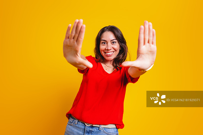 快乐的西班牙裔女性在黄色背景前顽皮地做手势图片素材