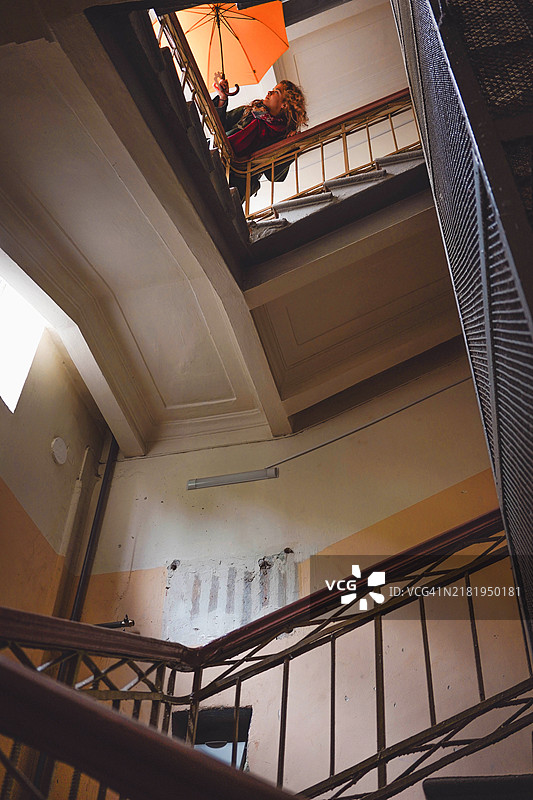 一位美丽的女性手持一把大黄伞，站在一座宏伟美丽的楼梯上。图片素材