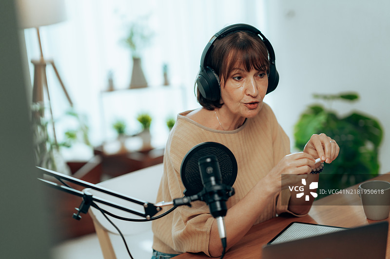 年长女性播客主持人在现代家庭工作室中使用专业麦克风录音图片素材
