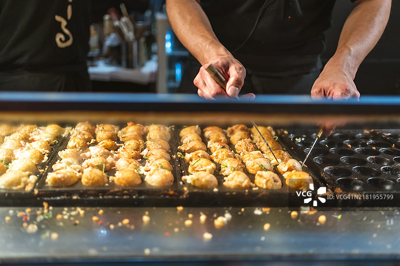 厨师在日本街头美食市场的热铁板上制作传统章鱼烧。图片素材