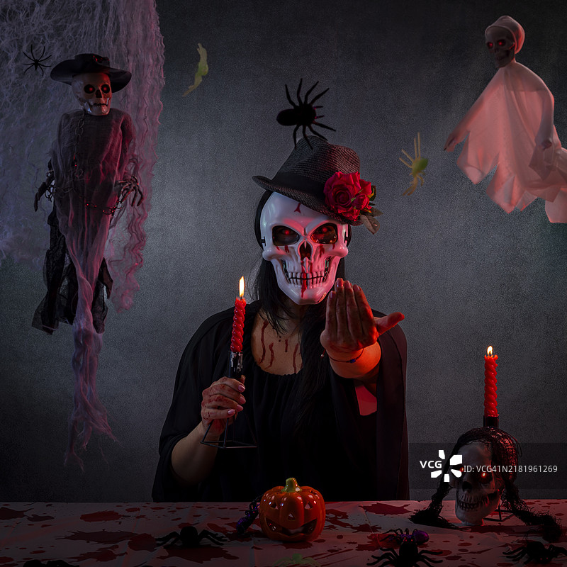 一位戴着骷髅面具和黑色斗篷的女人在激烈戏剧性的场景中邀请受害者参加她的仪式。图片素材