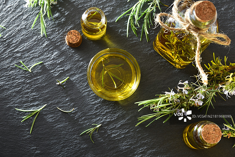 玻璃容器中的迷迭香油与新鲜的迷迭香枝在石板上图片素材
