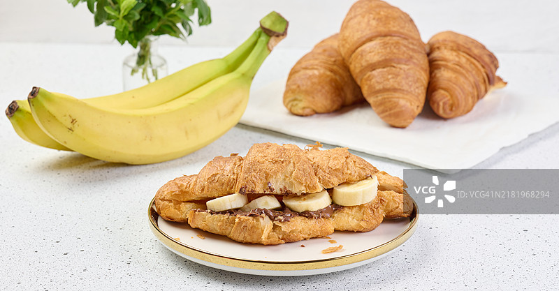 白色圆盘上的可颂面包，涂抹巧克力酱和香蕉片，早餐图片素材