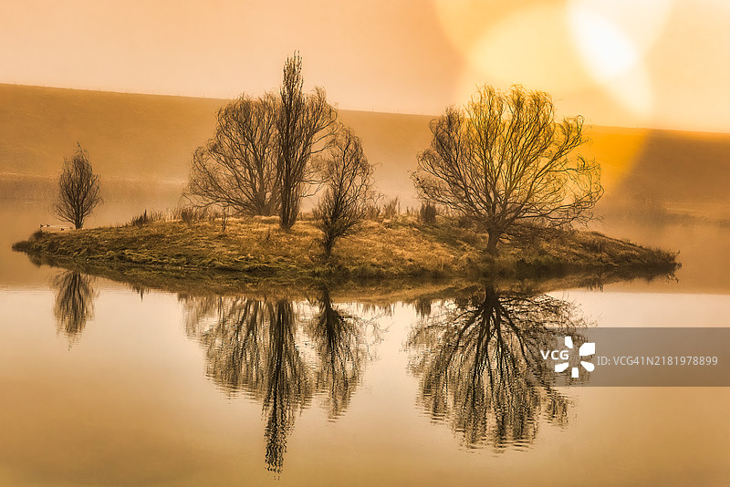 清晨薄雾中，小湖面上倒映出的岛屿和树木剪影图片素材