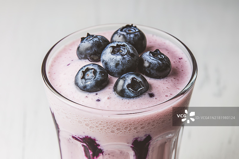 一杯蓝莓奶昔，上面放着新鲜的蓝莓，背景为白色。图片素材