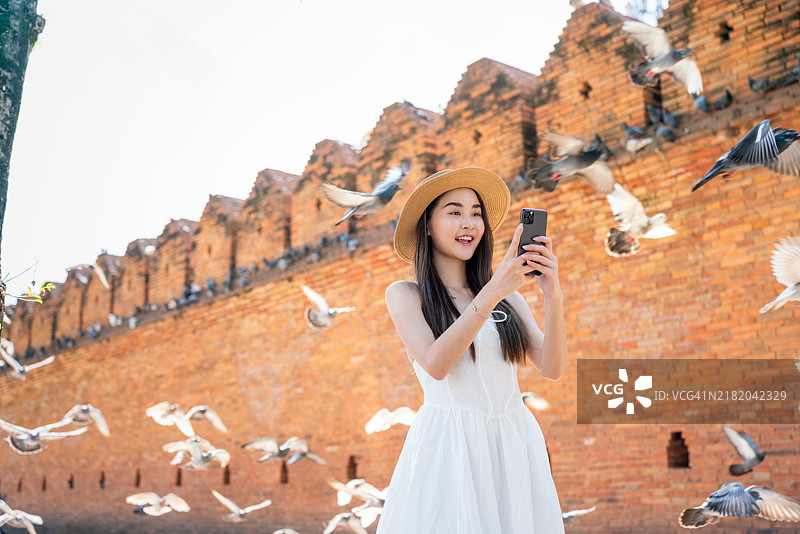 穿着夏季连衣裙的亚洲女性在泰国清迈的塔佩门使用智能手机图片素材