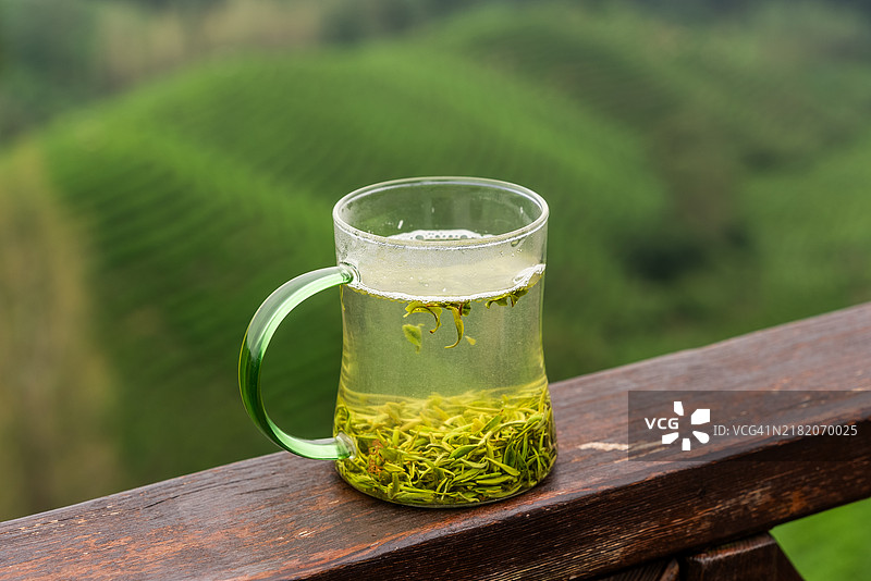 一杯泡好的绿茶放在茶叶种植区旁边图片素材