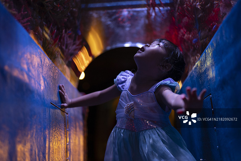 小女孩在海底水族馆中惊奇地凝视，脸上映出柔和蓝光下的迷惑与好奇。图片素材