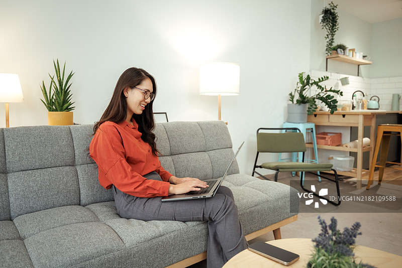 穿着休闲的美丽女性坐在家里的沙发上使用笔记本电脑图片素材