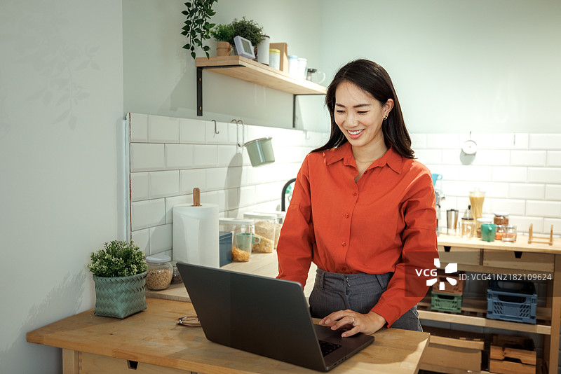 微笑的穿着得体的女性在家用厨房里使用笔记本电脑图片素材