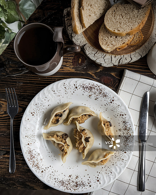 一盘自制饺子或波兰饺子，配有一杯深色液体和几片面包，摆放在质朴的木桌上图片素材