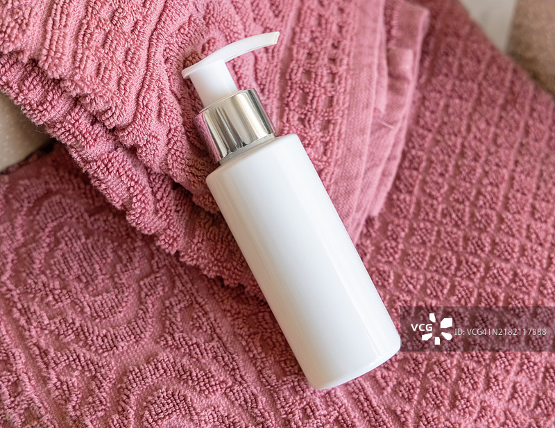 粉色折叠浴巾上的白色空泵瓶特写，化妆品样机图片素材