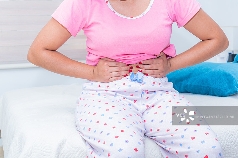 年轻女性坐在床上，手按着腹部的特写镜头图片素材