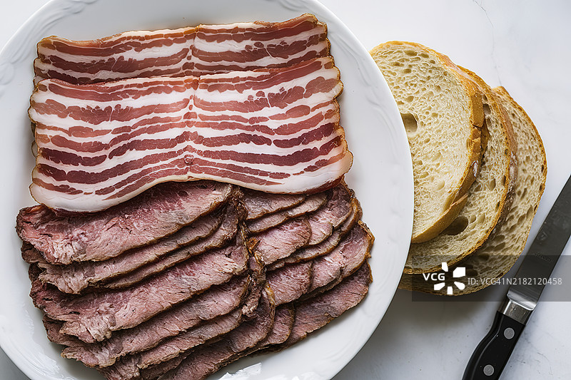 从上方俯视一只白色盘子，上面放着土耳其培根、熏牛肉和其他肉类切片。图片素材