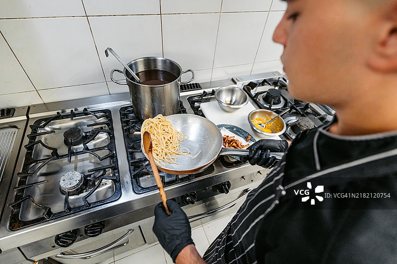 年轻厨师在商业厨房制作意大利培根奶酱意面图片素材