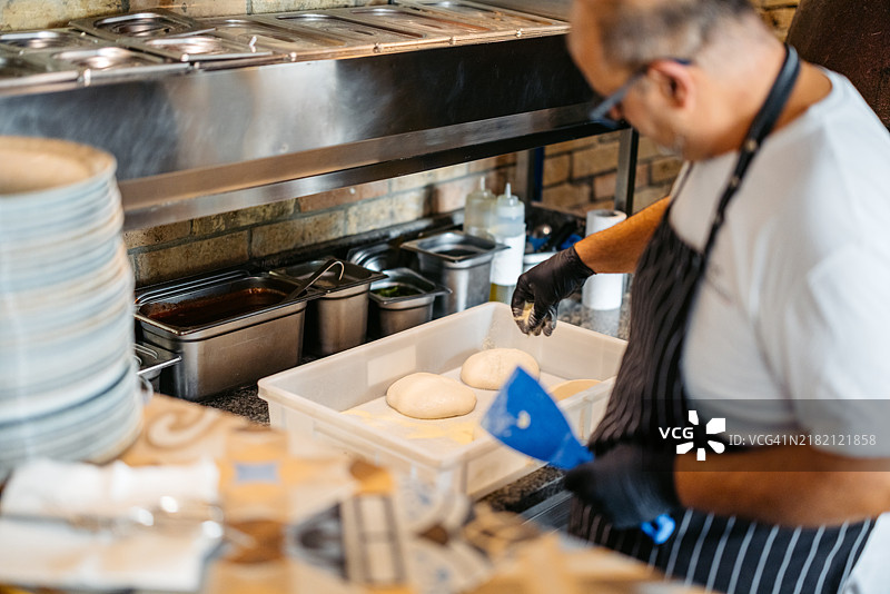 成熟的厨师在商业厨房中制作比萨饼面团图片素材
