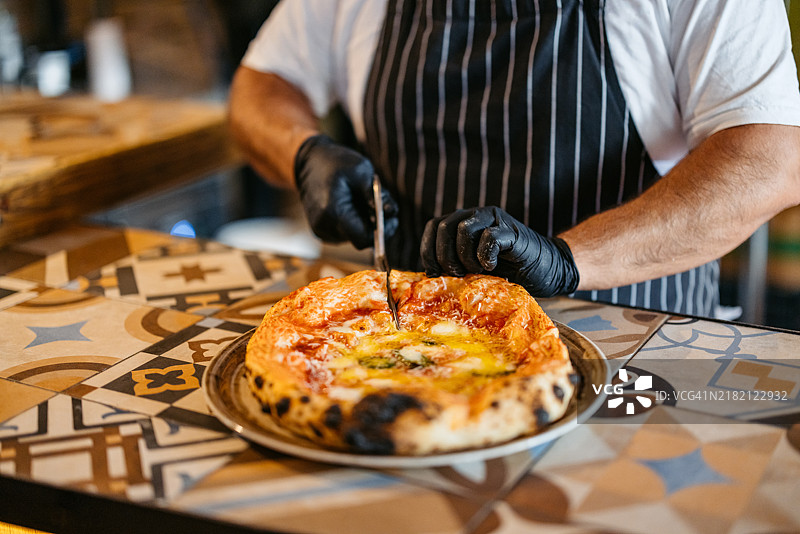成熟的厨师在商业厨房用剪刀切披萨图片素材