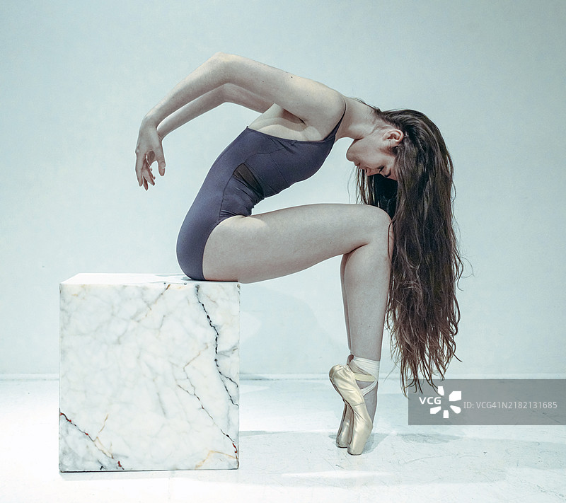 穿着芭蕾舞紧身衣和鞋子的年轻女性在石板上摆姿势，背景是墙壁，地点：美国伊利诺伊州芝加哥。图片素材