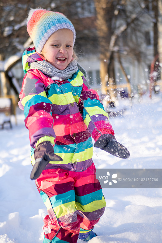 快乐的小女孩穿着五彩缤纷的冬装在雪地里玩耍图片素材
