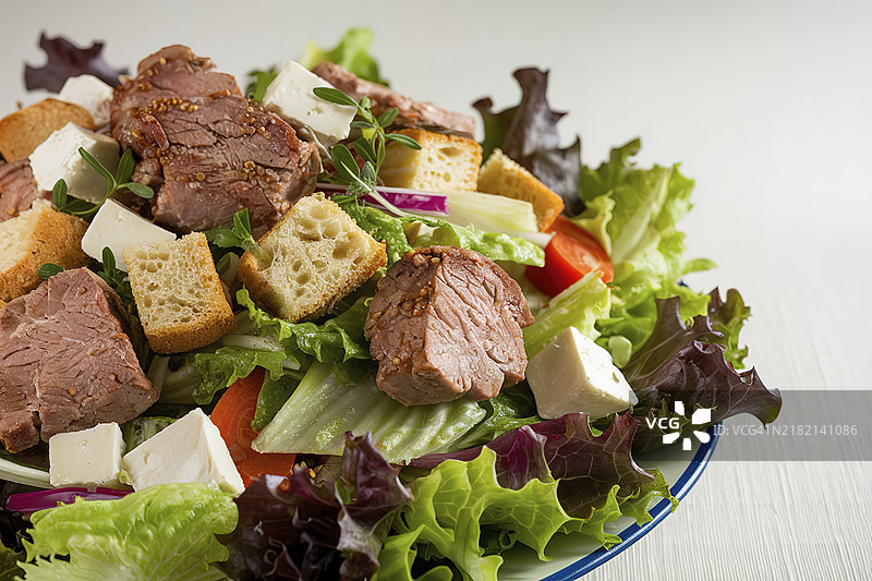 一只白色盘子里盛着混合蔬菜沙拉、肉块、面包丁和碎羊奶酪。图片素材