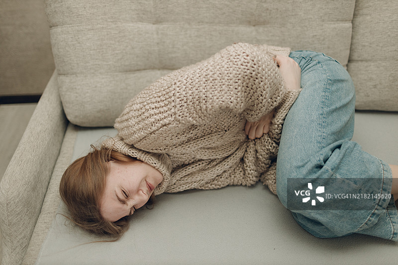 年轻女性因腹部疼痛躺在沙发上图片素材