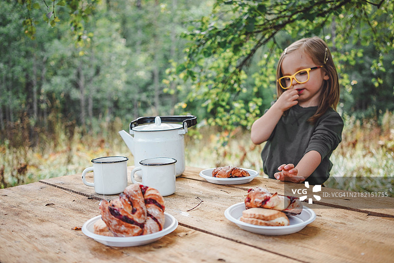 一个可爱的小女孩在森林露营时，享受着野餐，津津有味地吃着一个小面包。生态生活、与自然的和谐相处以及关爱环境。图片素材